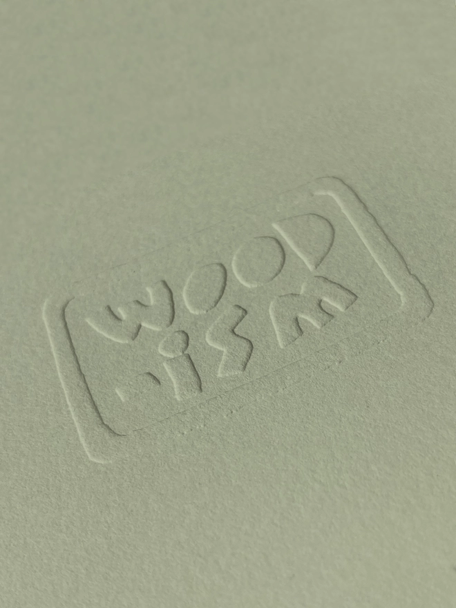 A close up on the embossed Woodism logo on the corner of the green print