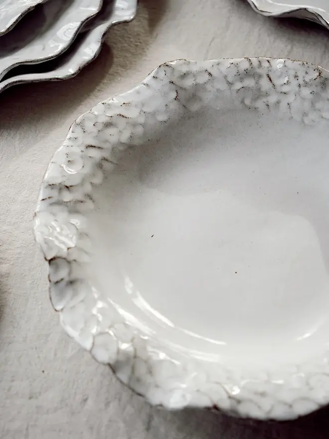 Dapple Stoneware Pasta Bowl, positioned next to other plates, placed on a table cloth. 