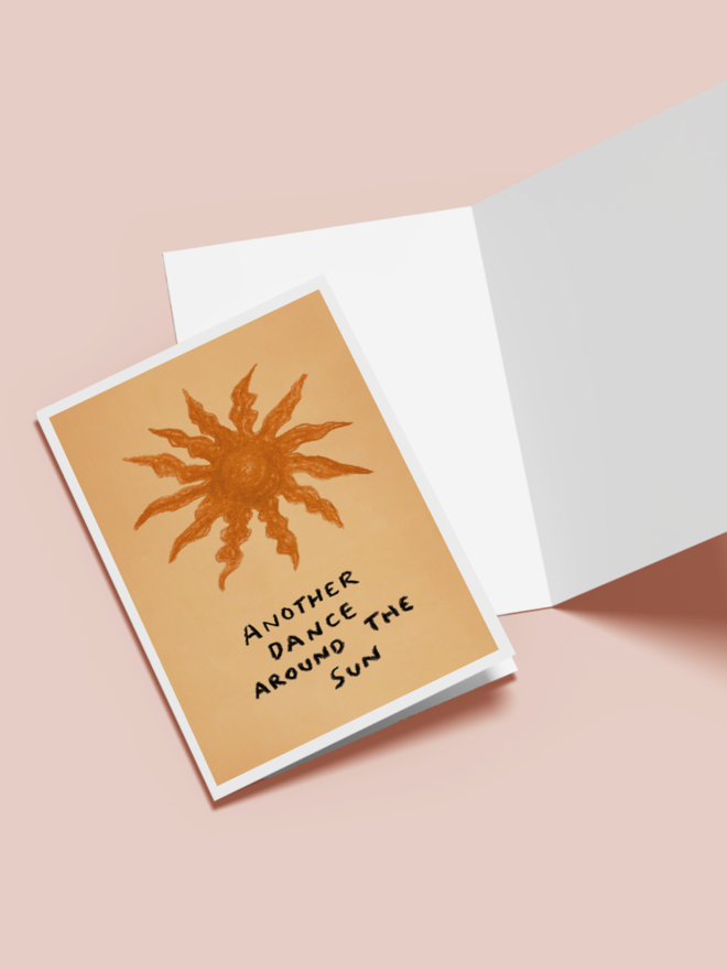 'another trip around the sun' card. an orange greetings card with an illustrated sun.