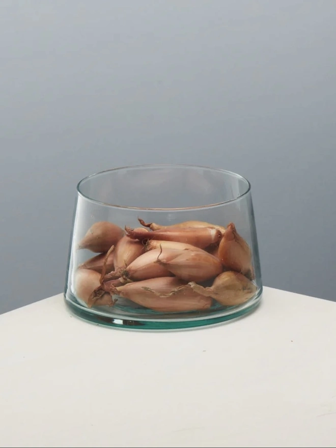 Tall Glass Dish, a tall glass dish sitting on a white surface against a baby blue backdrop. It is filled by food. 