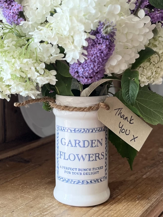  A tall handmade ceramic vase/jar is filled with flowers with a note saying thank you. 