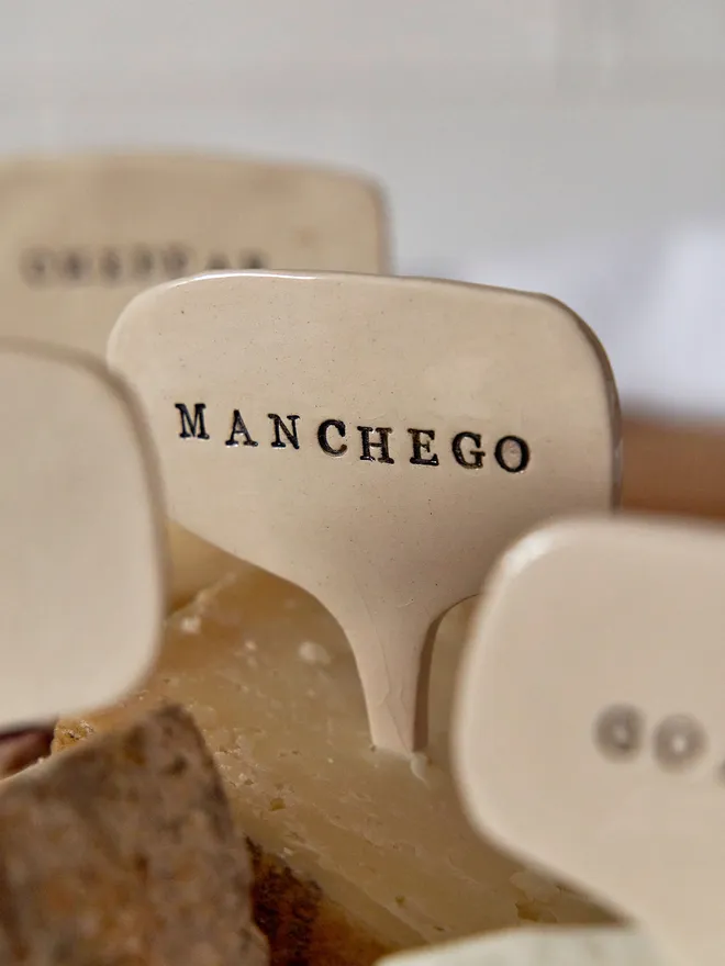 Ceramic cheese marker that reads Manchego on a wooden tray 