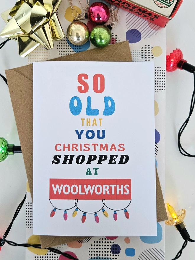 A photograph of the front of a humorous A6 greeting card illustrated using brightly coloured text and the retro shop logo. The text says so old you Christmas shopped at Woolworths with garland lights