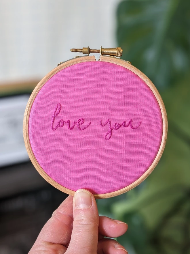 A hand stitched embroidery hoop with the words 'love you' on pink fabric