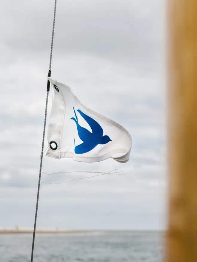 an ivory pennant flag with a blue swallow stiched on. its flying from a boat mast