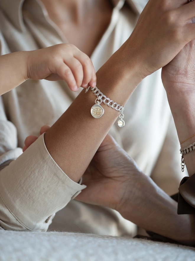 Hold tight charm on a chain bracelet on a model, with the child reaching out for Hold Tight