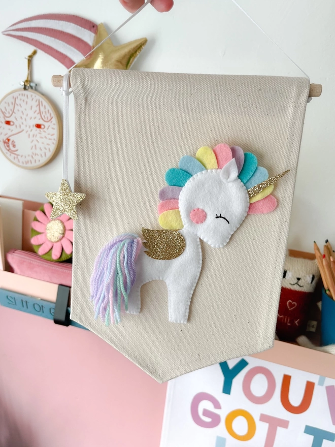 White unicorn with a pastel coloured mane and tail on a cream fabric banner