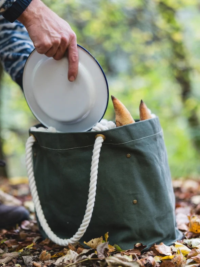  'the henley' canvas picnic bag. a canvas bag photographed on the ground, with plates and food being placed inside.