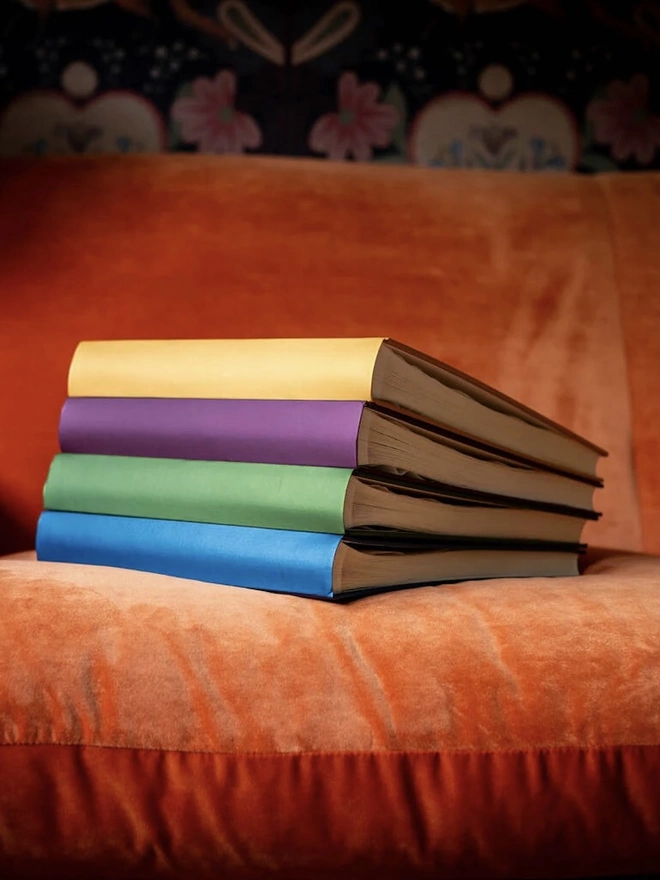 A stack of Personalised Large Wedding Guest Books With Two Names on an orange sofa. 