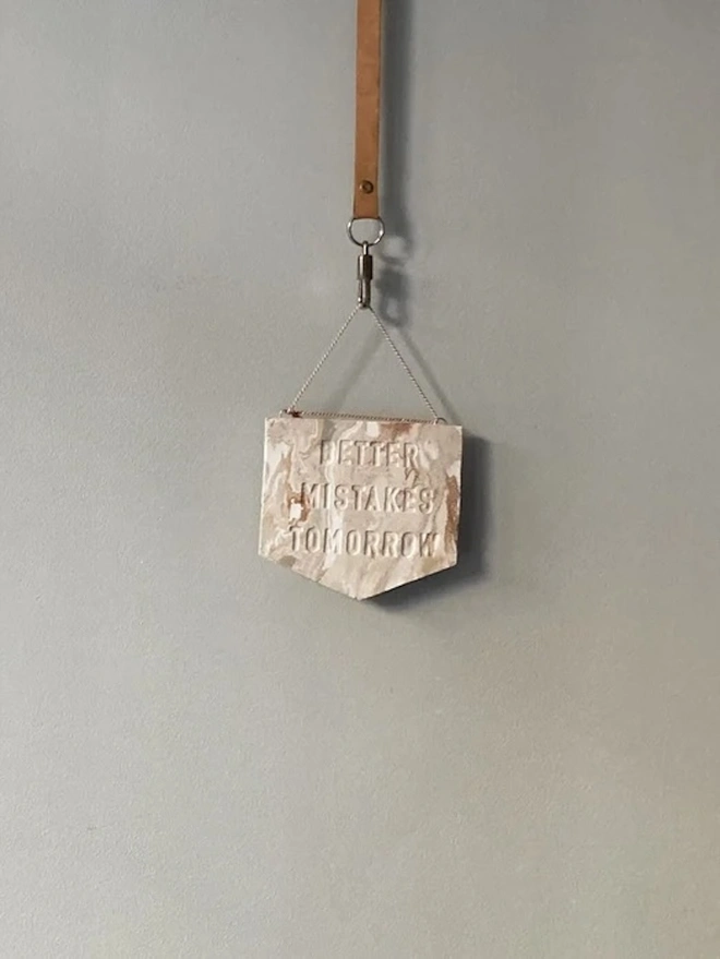 'Better Mistakes Tomorrow' Banner, a clay banner hanging against a plain backdrop.