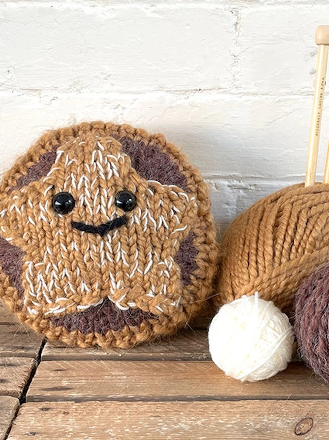 knitted mince pie with smiley face, next to spools of yarn
