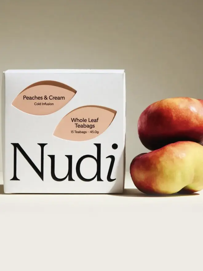 white box of peach tea with pale orange leaf design next to two peaches