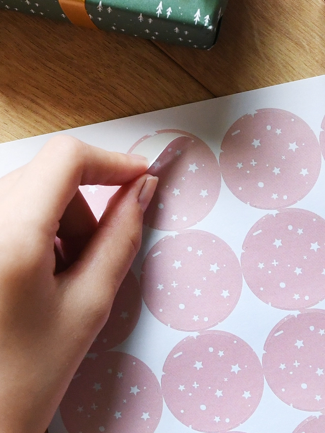 A hand is peeling a pink star design sticker from a sheet of 35 stickers.