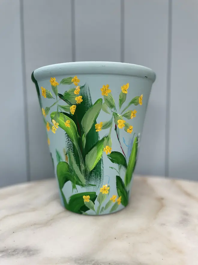 Unique hand-painted terracotta pot featuring yellow cowslip flowers on a pale blue background