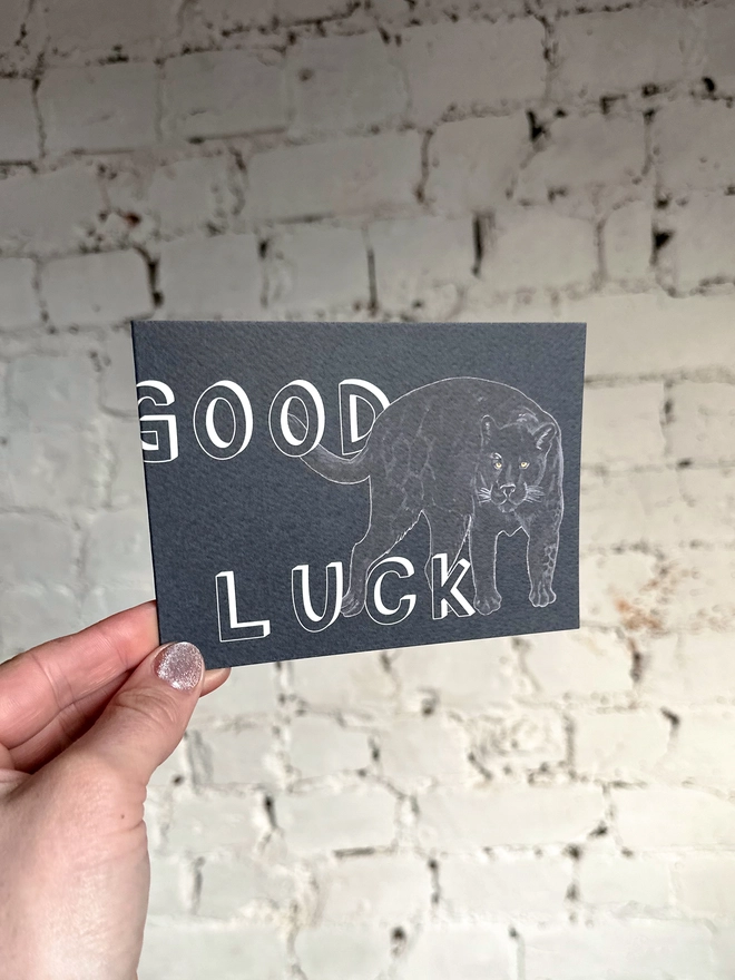a dark grey greetings card featuring an illustration of a black panther with the text “good luck”