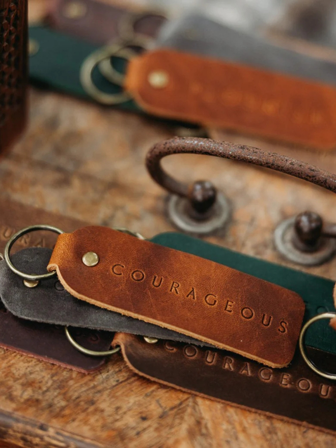encouraging leather keyring. brown keyrings laid atop a blanket, embossed with the word 'courageous'.