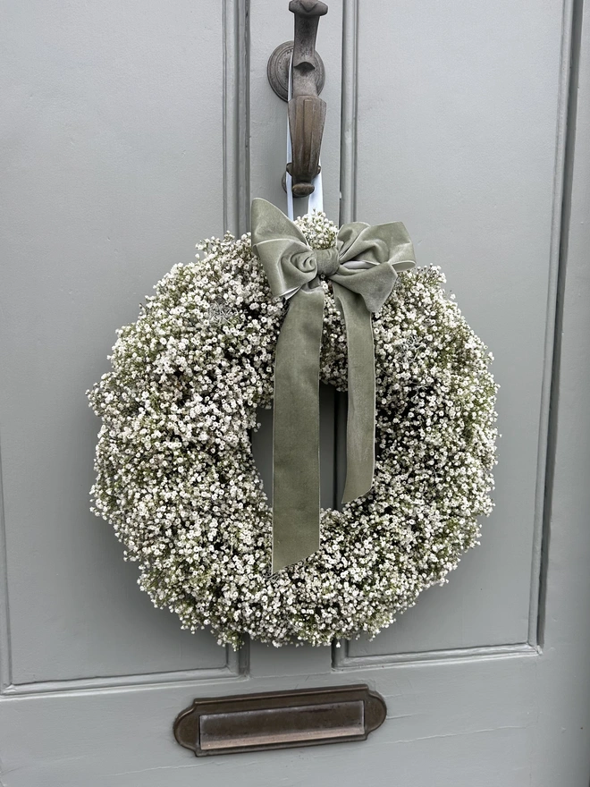 Fresh White Gypsophila Wreath with a Green Velvet Bow hanging on a grey door