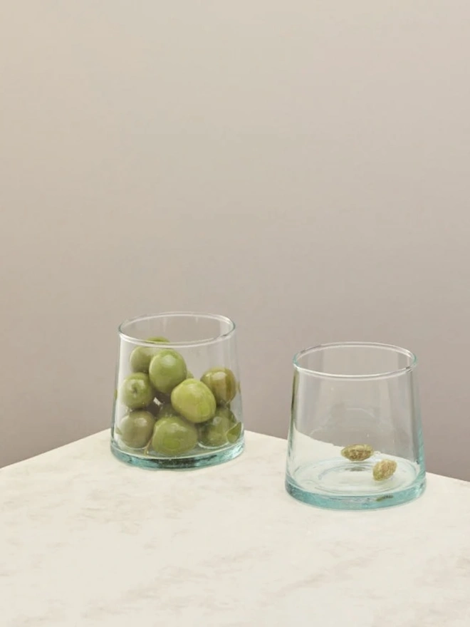 Low Glasses (Set Of 1 Or 4), a low glass sitting on a white counter top against a plain backdrop. It is filled by some olives. 
