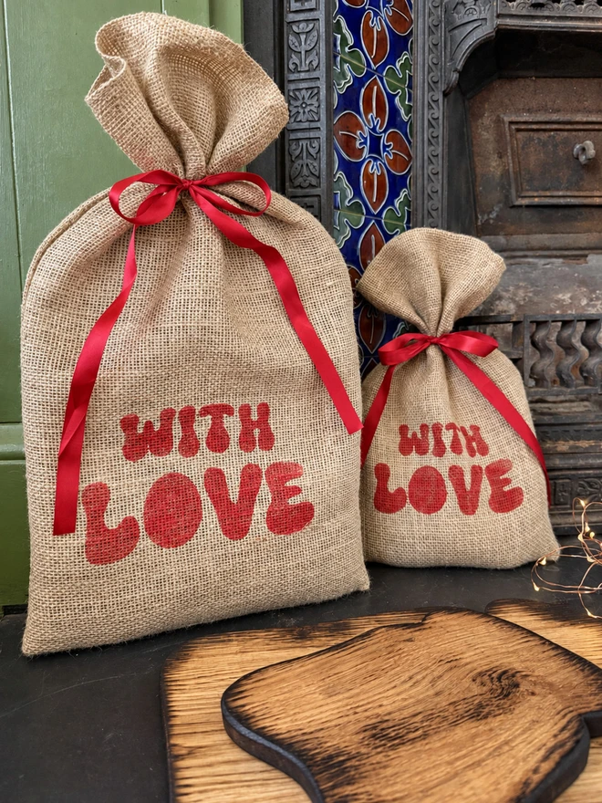 Large and small reusable jute gift sack printed WithLove and tied with red ribbon.Background fireplace 