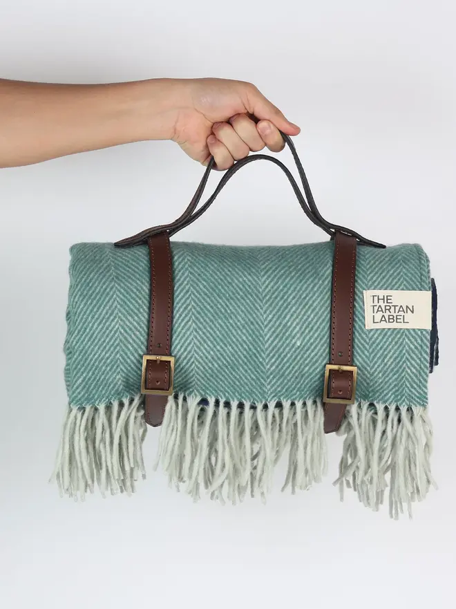 Pistachio Recycled Wool Tartan Blanket, a person holding a blue picnic blanket against a white backdrop. 