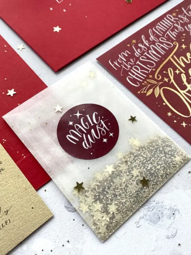 A glassine packet of silver glitter and gold stars with a burgundy "Magic Dust" sticker.