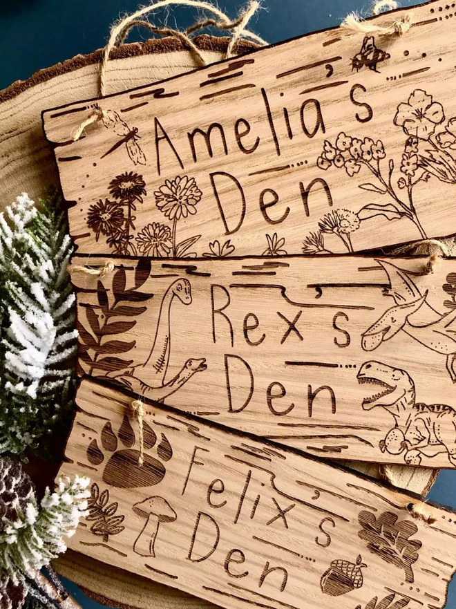 Personalised Wild Flowers Den Sign, Three stacked wooden signs showing design options: "Amelia's Den" with flowers, "Rex's Den" with dinosaurs, and "Felix's Den" with woodland items.