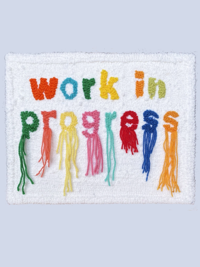 work in progress written in bright colours in wool in lower case type on a white background threads hang down from the word "progress"