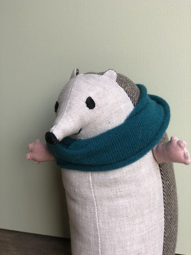 Handmade fabric toy hedgehog made from natural linen (front) and brown herringbone tweed (back), wearing a blue lambs wool scarf. With embroidered eyes, nose and smile.