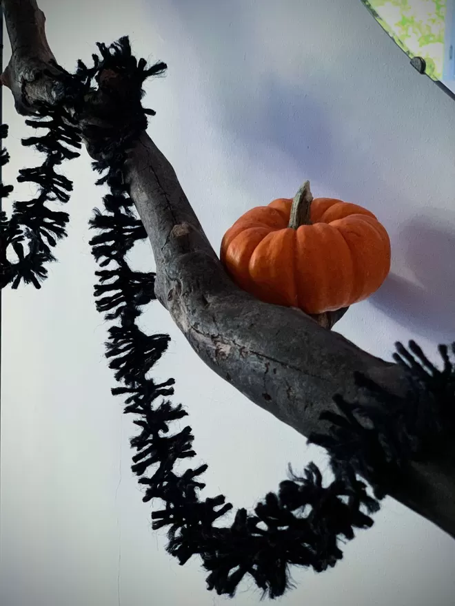 Black Jute Spider Leg Strinsel (string tinsel) draped off a branch alongside a small pumpkin against a white background