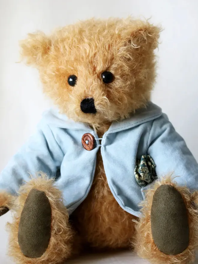 Handmade teddy bear with soft textured fur, wearing a blue jacket, posed against a plain background.