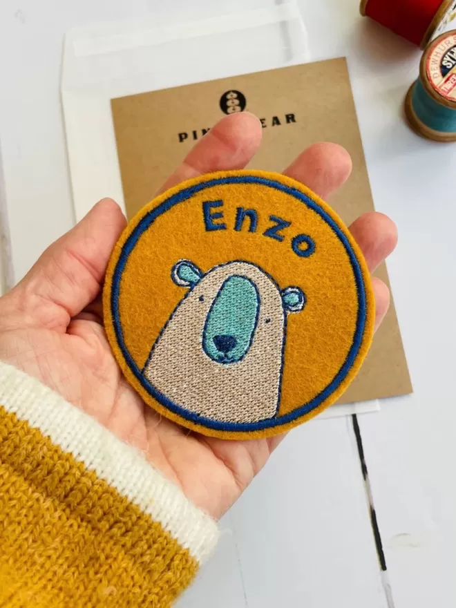 A personalised embroidered bear name patch being held in a hand.
