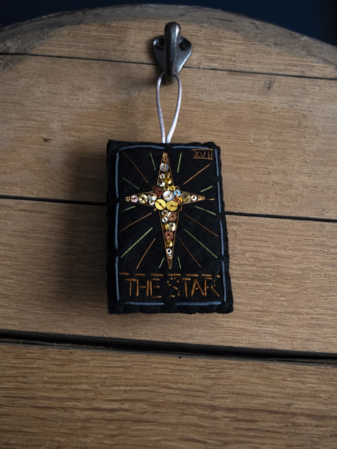 A handcrafted felt ornament with sequins and embroidery depicting "The Star" tarot card. 