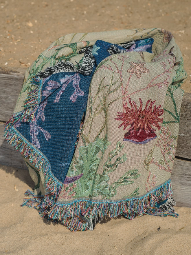 'Intertidal Sand' Recycled Cotton Blanket seen on a wooden plank on the beach.