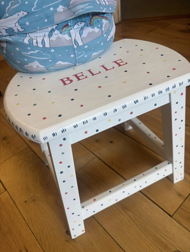 Child sitting on their Christening wooden stool with polka dot design. 