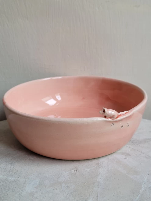 a pink ceramic cat bowl with a miniature pink mouse attached on the edge with little paw prints on the side of the dish