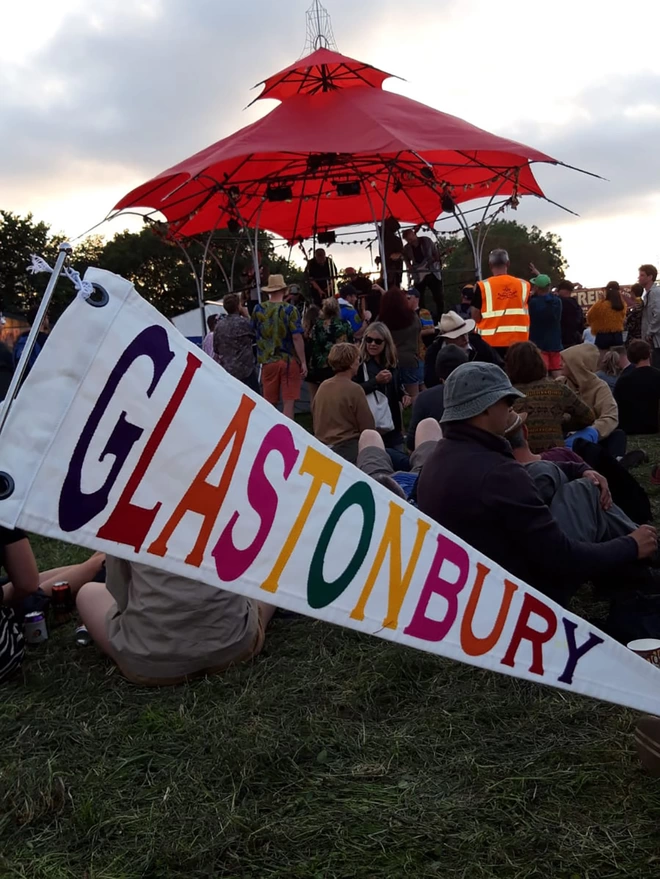 An ivory canvas Glastonbury pennant flag with multi coloured letters at the festival.