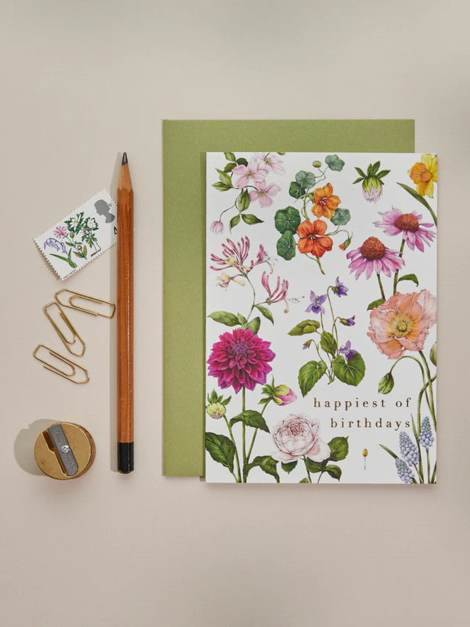 'Happiest Of Birthdays' Illustrated Floral Card. a white floral card and green envelope photographed against a plain background.