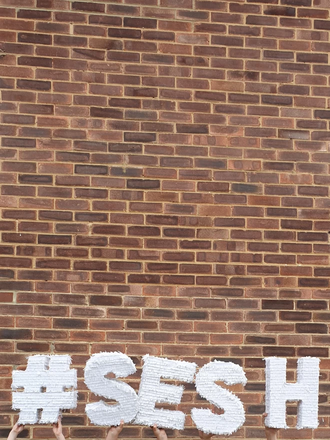 white letter pinatas spelling out #SESH in front of a brick wall
