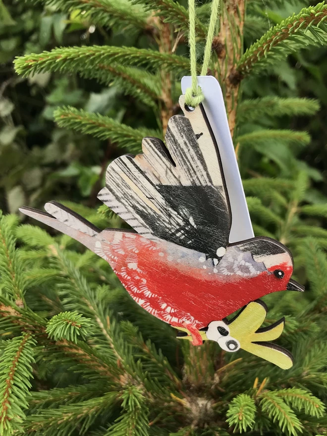 An illustrated Robin decoration hangs in the fresh green branches of a fir tree