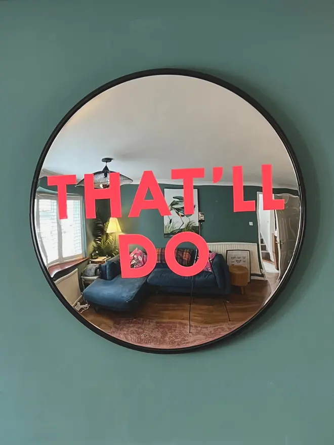 Round convex mirror with 'That'll Do' handpainted in neon pink on a teal wall