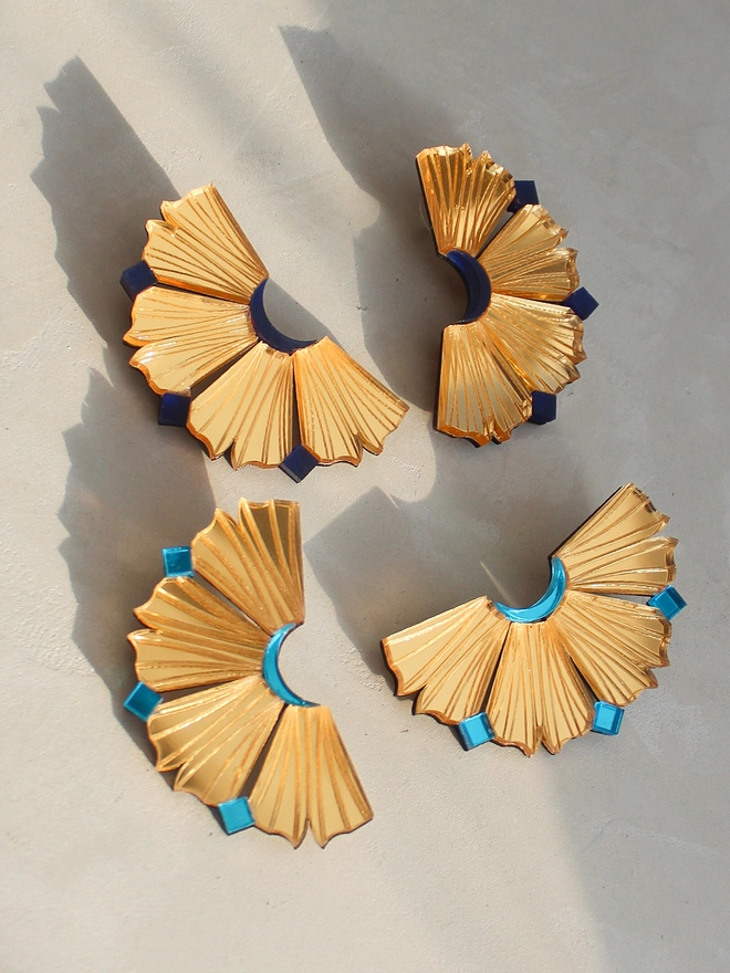 A still life image of 2 pair of earrings with different colourways. One with Navy and other with Aqua. There's soft shadows behind the earrings.