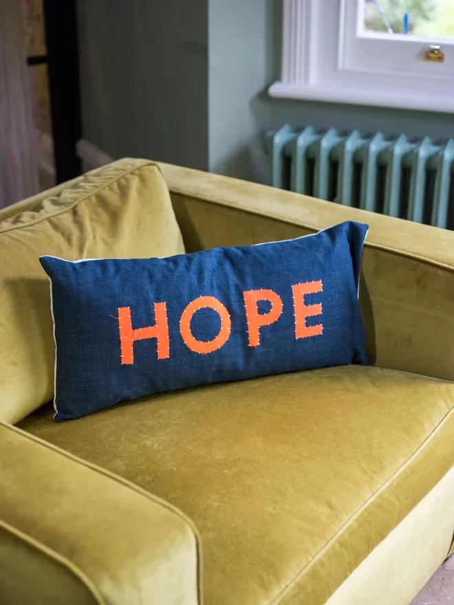Her Story Cushion - HOPE seen on a yellow velvet chair.