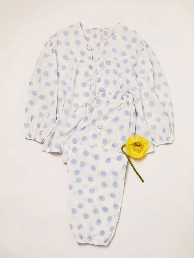 White and pale blue pyjama set laying flat with a yellow flower sitting on top