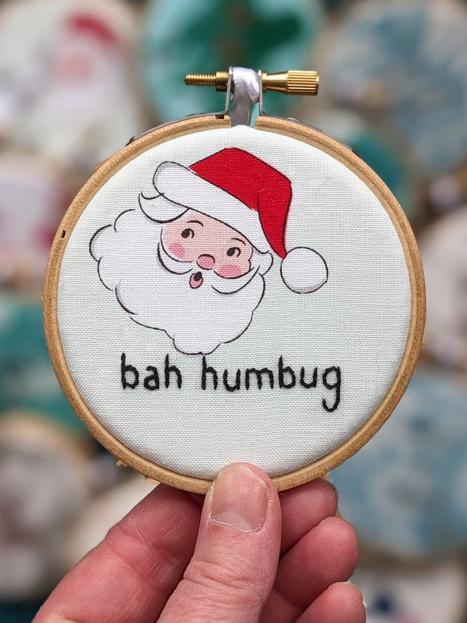 A hand embroidered hoop on Christmas fabric reading bah humbug