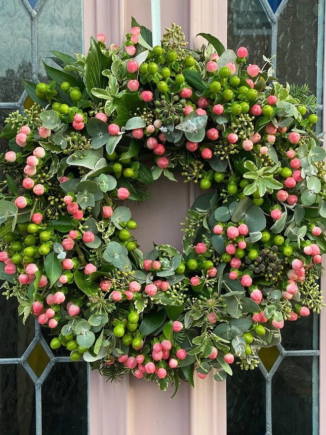 Floral hypericum door wreath. a green floral wreath featuring leaves and buds hung on a beige door.