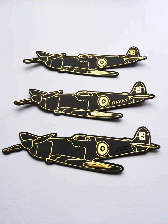 three black leather bookmarks of a spitfire airplane in gold foil embossing from the number 19 squadron from World War Two