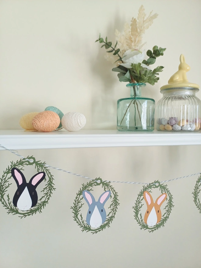 5 Bunny Easter Paper Garland hung from white shelf decorated for easter. Black, Grey and Toffee coloured bunnies with white noses and pink ears.