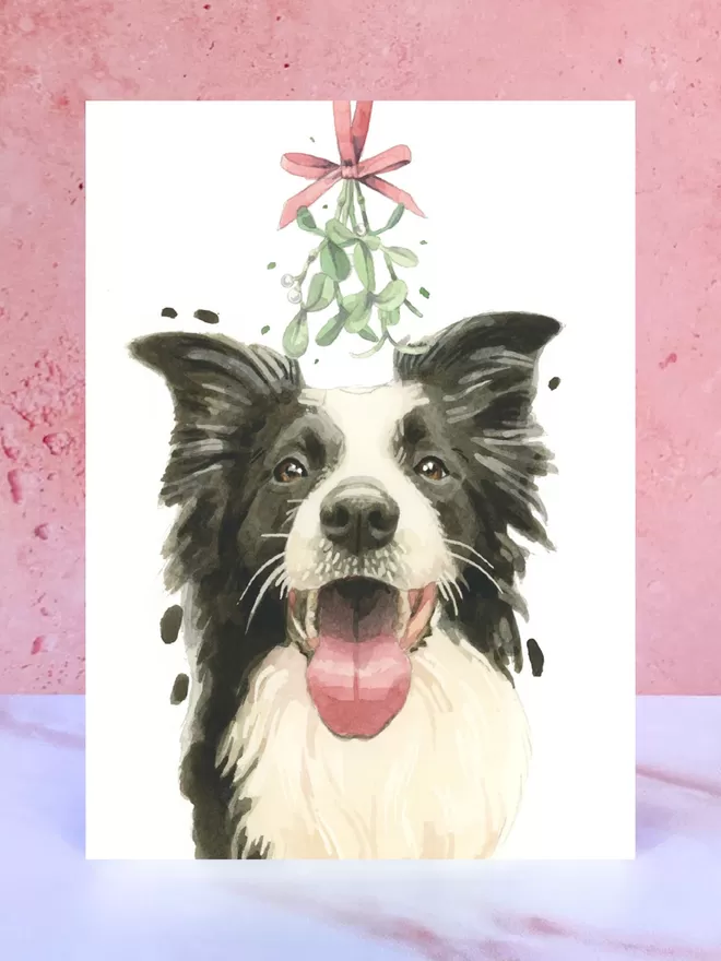 A Christmas card featuring a hand painted design of a Collie, stood upright on a marble surface.