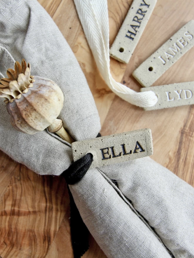 Ceramic name tag tied around a beige napkin with black ribbon