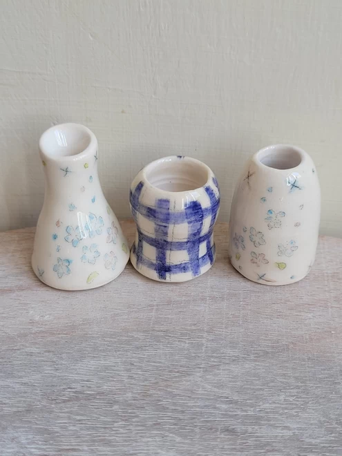 tiny miniature ceramic vases in a row on a wood surface with hand painted blue checks and flowers on the pots 